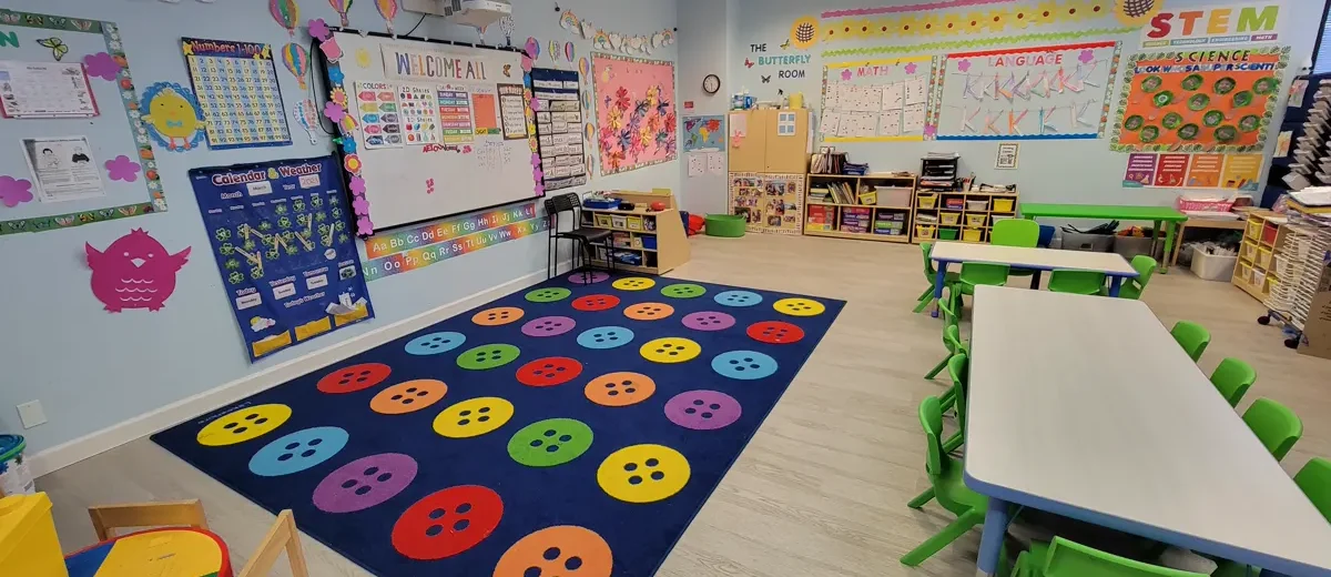 Bright preschool classroom at The Little Butterflies with a colorful circle-time rug, child-size tables, and STEM, math, and language wall displays