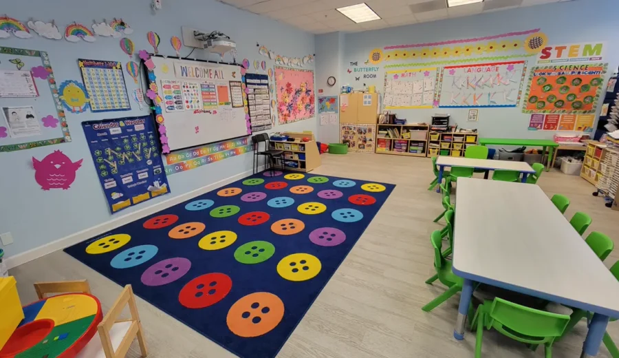Bright preschool classroom at The Little Butterflies with a colorful circle-time rug, child-size tables, and STEM, math, and language wall displays